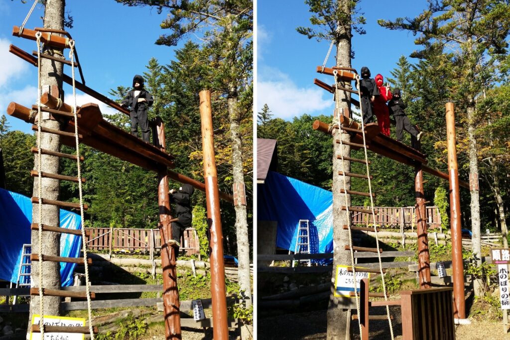 Two images of children dressed in ninja outfits climbing and standing on a wooden high ropes structure. In the left image, a child in black stands confidently on the platform while another climbs the ladder. In the right image, three children, two in black and one in red, stand together on the platform at the top of the structure. The background features trees and a blue tarp covering part of the area.