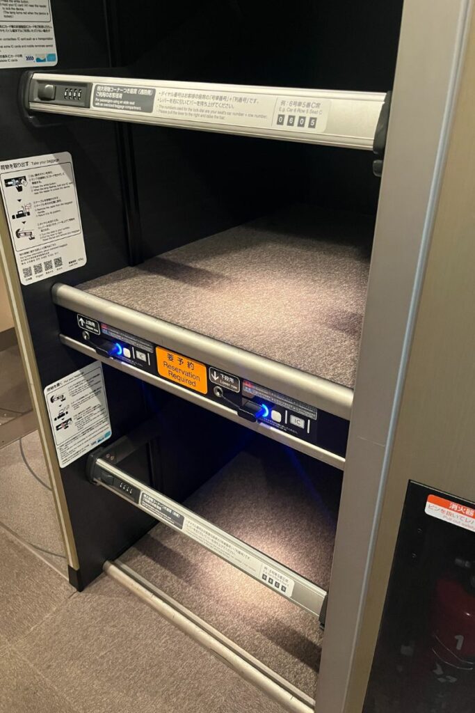 A close-up of a baggage storage compartment on the N700 Shinkansen, featuring multiple shelves with locks and reservation indicators. The signage provides instructions for use and emphasizes the need for reservations.