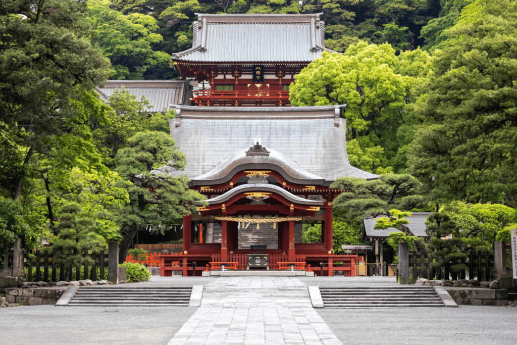 Tsurugaoka Hachimangu Shrine in Kamakura, Japan, stands prominently with its bright red facade and curved rooftops framed by lush greenery. The shrine's architectural details are highlighted by intricate wooden carvings and traditional lanterns, creating a peaceful and historic ambiance.