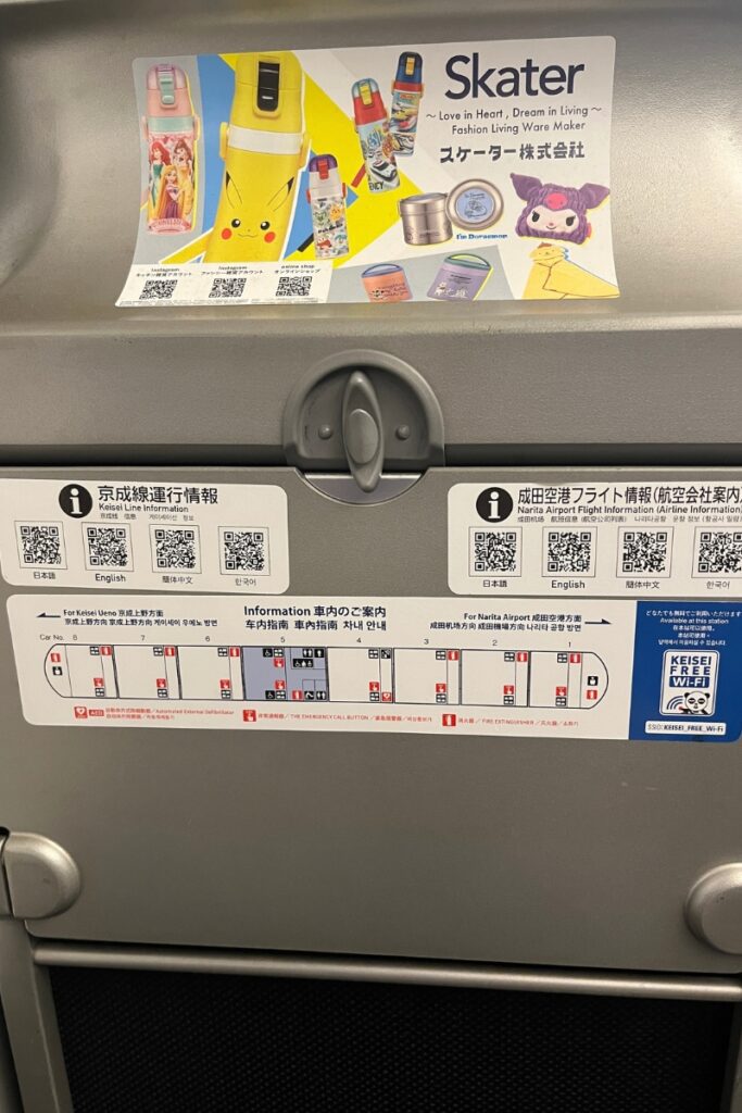 A close-up of the back of a train seat in the Keisei Skyliner, showing a folded tray table with various informational stickers. The stickers provide details about the train's layout, emergency exits, Keisei line and Narita Airport flight information, and instructions in multiple languages. QR codes for accessing additional details and free Wi-Fi are also visible. Above the tray table, an advertisement for Skater brand products features colorful drink bottles, including ones with Pikachu and Disney princess designs.