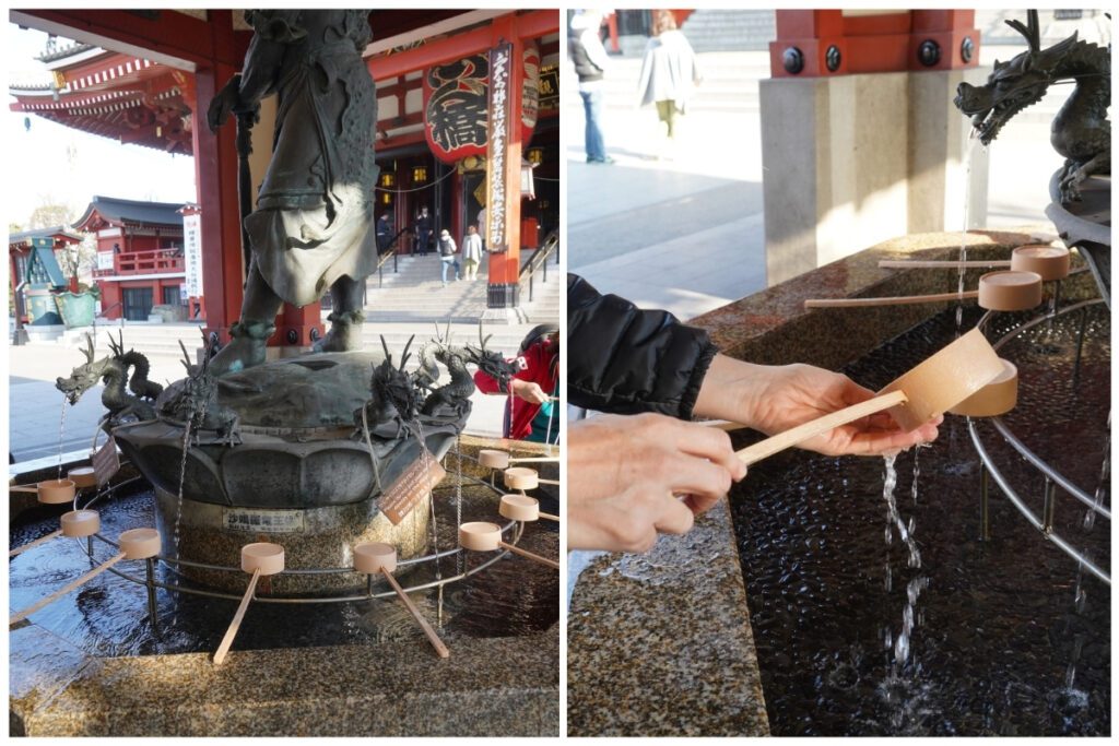 A purification fountain, or temizuya, in front of Sensō-ji Temple in Tokyo, features dragon-headed spouts pouring water into a stone basin. Wooden ladles rest around the edge, while a person demonstrates the ritual cleansing by rinsing their hands, a symbolic act of purification before entering the temple. The grand red lantern and temple steps are visible in the background.