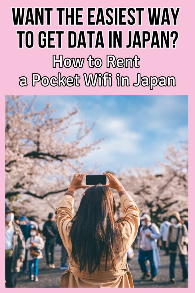 Woman with long brown hair holds up her phone to take a photo of cherry blossoms in full bloom, surrounded by people in a park in Japan. Text overlay on a pink background reads "Want the easiest way to get data in Japan? How to Rent a Pocket Wifi in Japan."