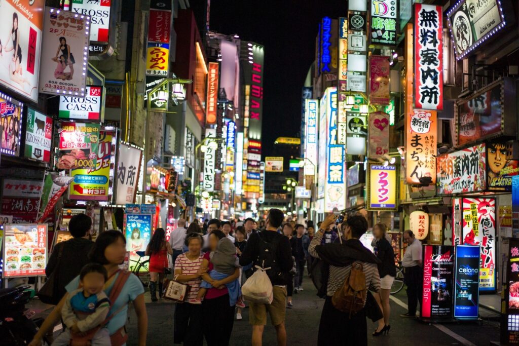 Crowded Kabukicho street at night lined with neon signs and lit storefronts in Shinjuku, Tokyo.
