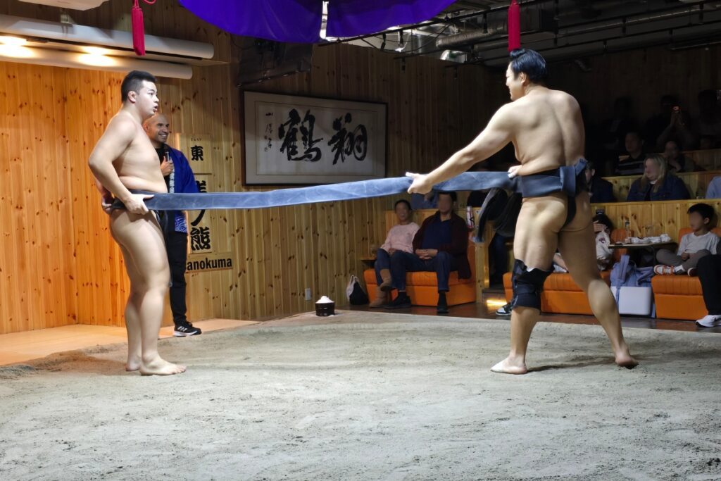 Two sumo wrestlers demonstrating the mawashi rule at Asakusa Sumo Club, Tokyo, where a fully detached belt means instant loss.