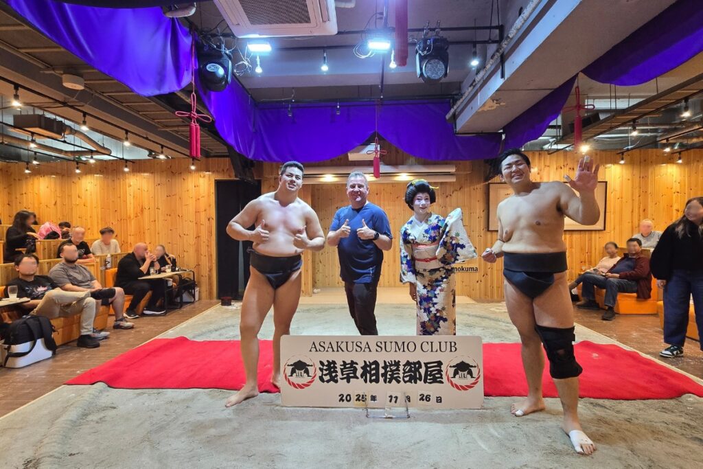 Author posing with two sumo wrestlers and a kimono-clad performer on the ring at Asakusa Sumo Club.