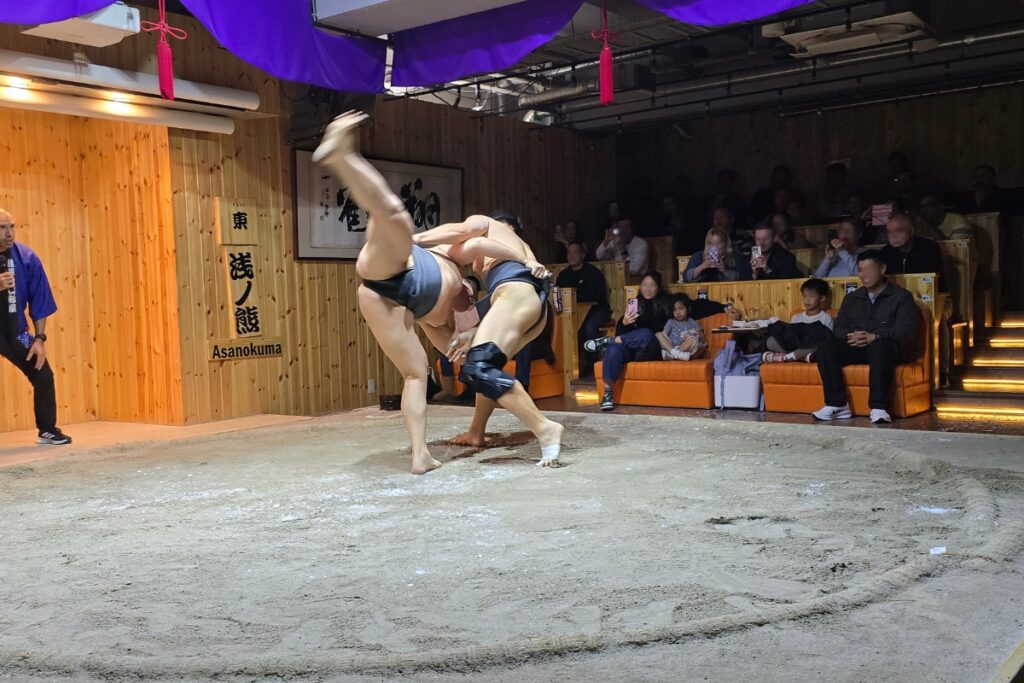 Sumo wrestler attempting an overhead throw during a bout on the sand ring at Asakusa Sumo Club, Tokyo.
