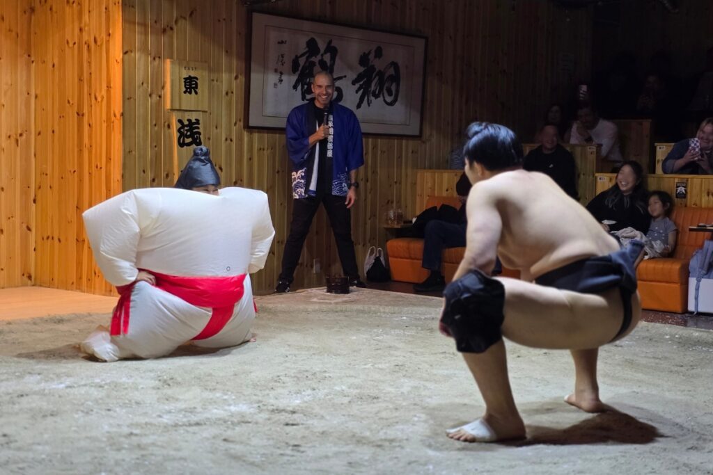 Guest in an inflatable sumo suit facing a sumo wrestler on the ring at Asakusa Sumo Club, Tokyo.