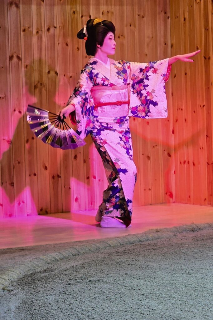 Performer in a floral kimono dancing with a fan on the sumo ring stage at Asakusa Sumo Club, Tokyo.