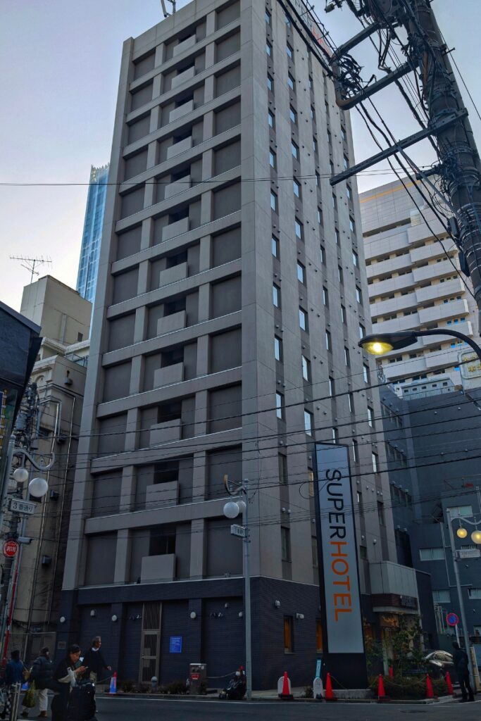 Super Hotel Shinjuku Kabukicho exterior tower with vertical signage on a street corner at dusk.